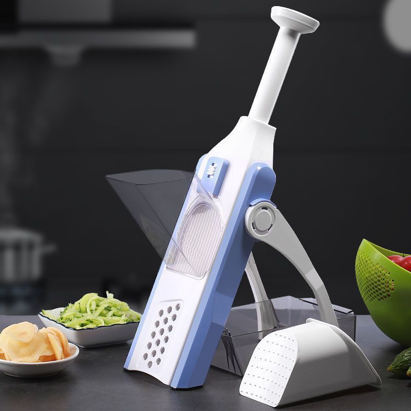 The image shows a kitchen counter with a bowl of vegetables, a plate of food items, and a mandolin slicer on it. The background is slightly blurred, giving the focus to the kitchen tools on the counter.