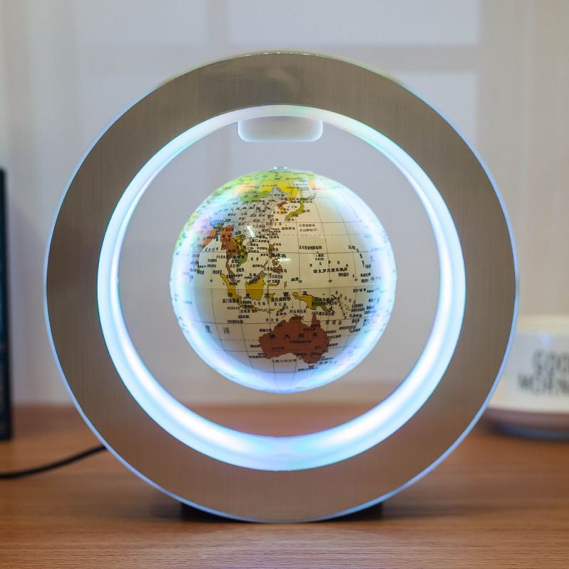 The image shows a 3D illuminated globe on a wooden table, with a wire connected to it. On the left side of the table is a black object, and on the right side is a white object. In the background is a wall.