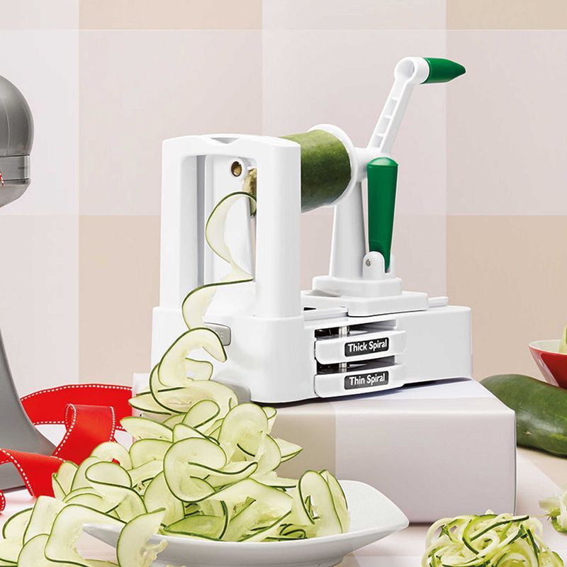 The image shows a kitchen counter with a bowl of sliced cucumbers next to a mandolin slicer. On the counter, there are also a few other objects, and in the background, there is a wall.