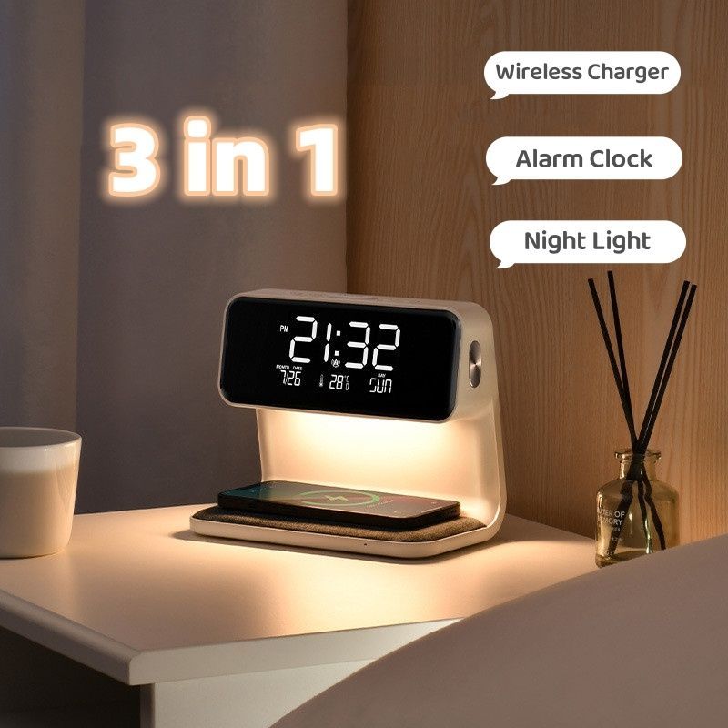 The image shows a digital alarm clock sitting on top of a nightstand next to a cup of coffee, a mobile phone, a book, and a glass with sticks in it. On the right side of the image, there is a bed, and in the background, there are some text on the wall. The alarm clock has a LED display, making it easy to read the time.