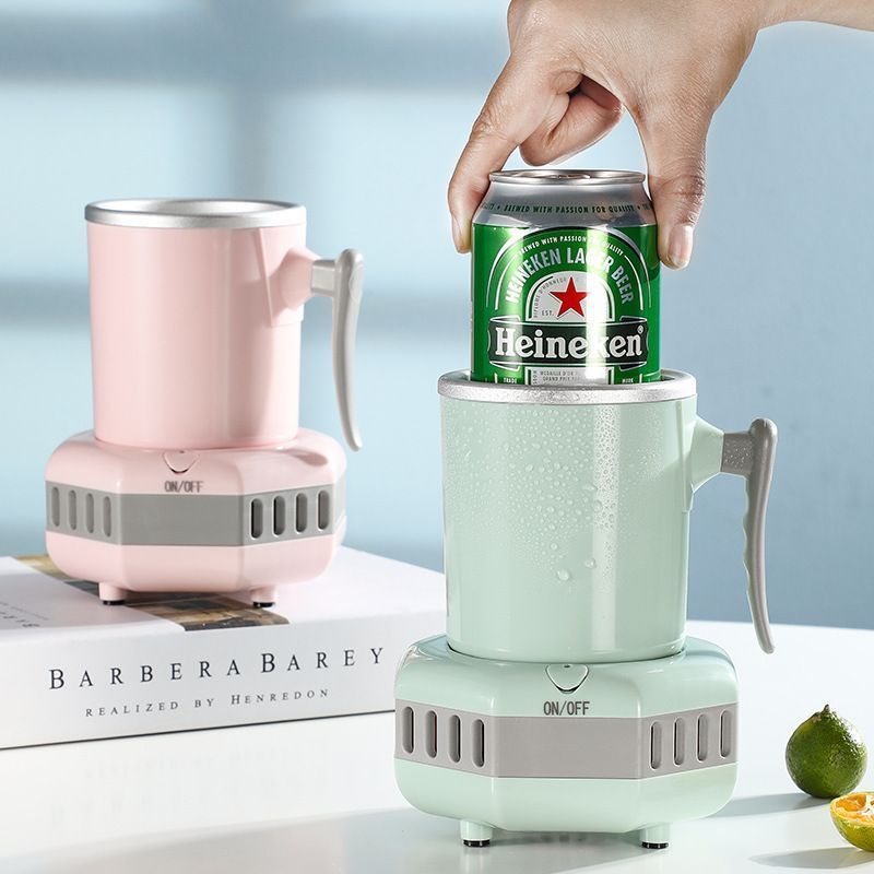 The image shows a person's hand holding a can of beer in front of a barbera barey mini blender, which is sitting on a table with a lemon and a box beside it. The background is slightly blurred, giving the image a dreamy feel.