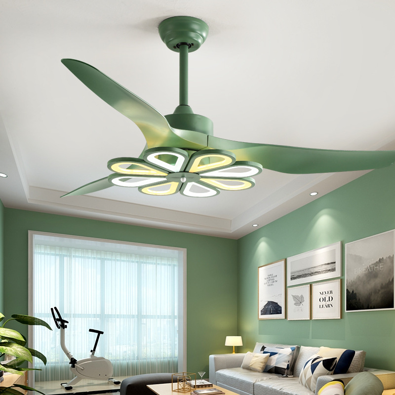 The image is of a ceiling fan with a green color. The fan has four blades, each with a unique design. The blades are arranged in a fan-like pattern, with the largest blade at the top and the smallest at the bottom. The center of the fan has a circular light fixture with a yellow and white flower-like design in the center. The light fixture is attached to the ceiling with a small green knob. The background is white, making the fan stand out.