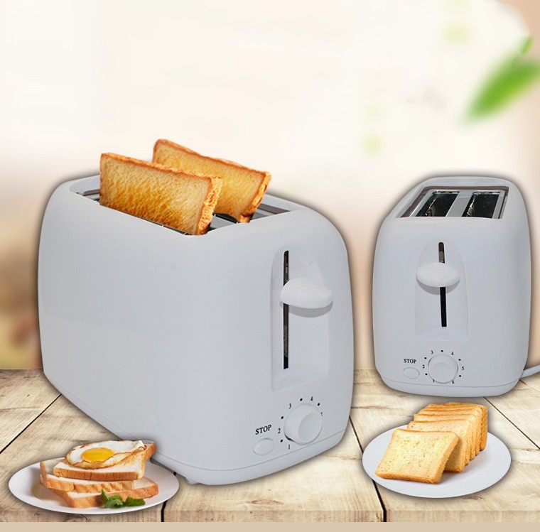 The image shows two toasters on a wooden table. The toasters are white in color and have a sleek design. On the left side of the image, there is a toaster with two slices of bread in it, and on the right side, there are two slices with a fried egg on top. There is also a small plate with more bread on it. The background is blurred, but it appears to be a kitchen countertop with a plant in the corner.