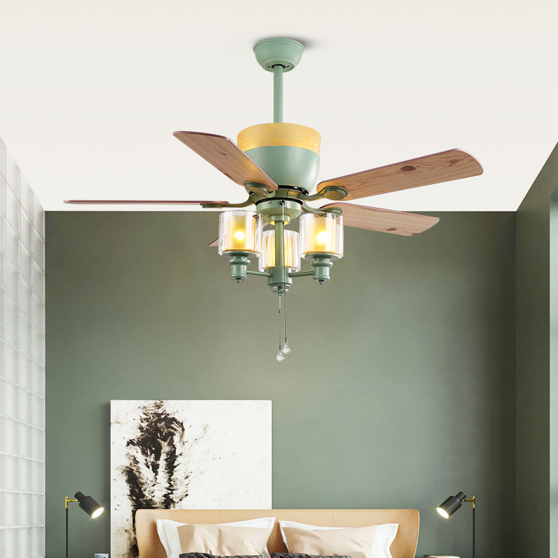 The image is of a ceiling fan with a light fixture. The fan has four blades, each with a different color - green, yellow, and brown. The blades are arranged in a fan-like pattern, with the green blades on the top and the yellow blades in the middle. The light fixture is attached to the ceiling with a green light fixture at the top. Below the light fixture, there are three small glass shades with a gold-colored metal frame. The glass shades are attached to a metal rod at the bottom, which is likely used to hang the fan. The overall design of the fan is modern and elegant.