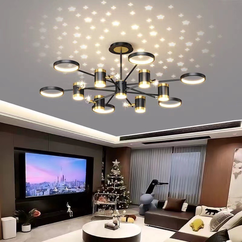 The image shows a modern chandelier with a unique design. It has a black metal frame with multiple circular lights hanging from it. The lights are arranged in a circular pattern, with each light having a different size and shape. The light fixture is suspended from the ceiling, creating a star-like effect. The dimensions of the light fixture are 120cm in length and 120cm wide. The background of the image is a gray wall with a red stripe on the top left corner.