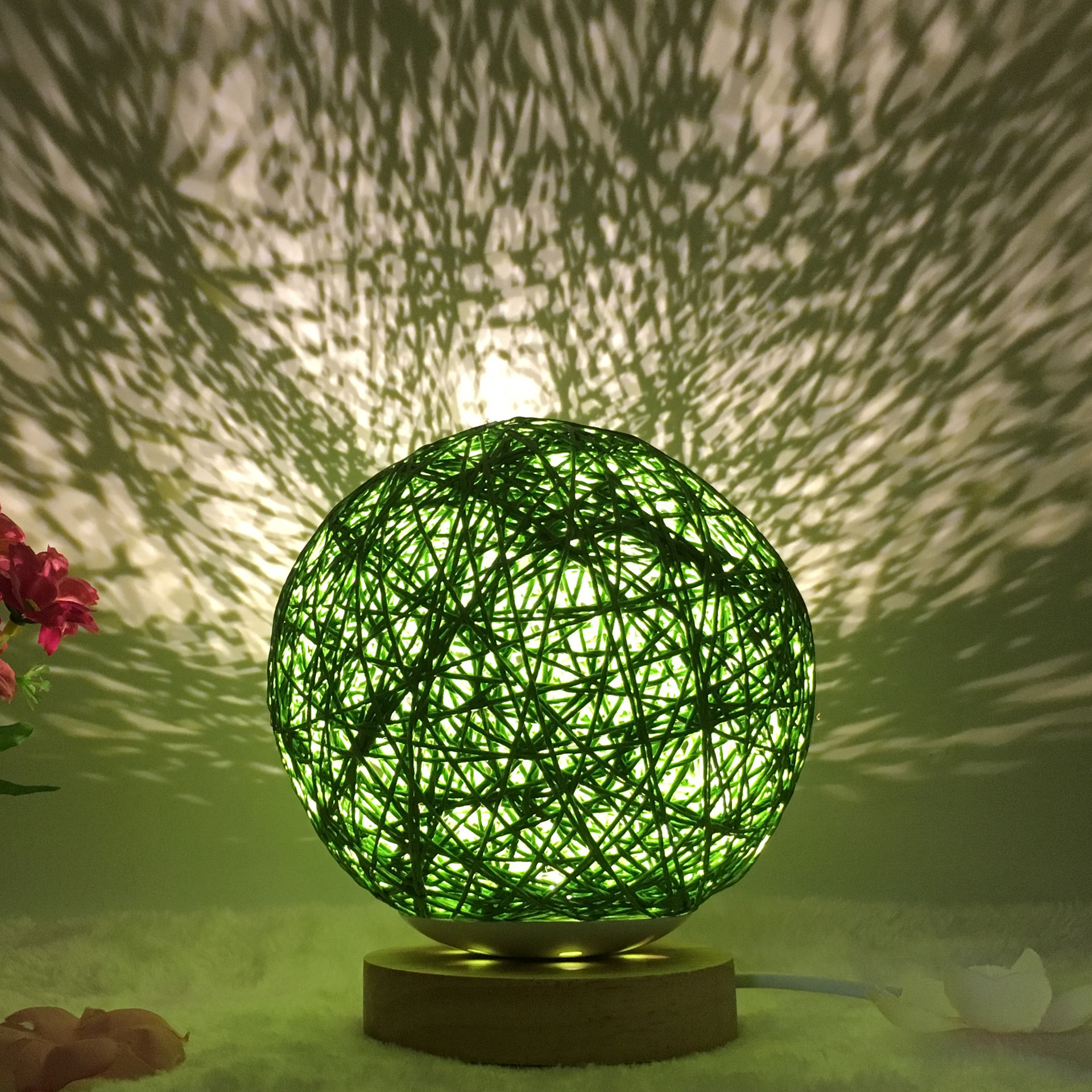 Green Creative Rattan Ball Lamp with handwoven shade on wooden stand, casting decorative shadow patterns on the wall.