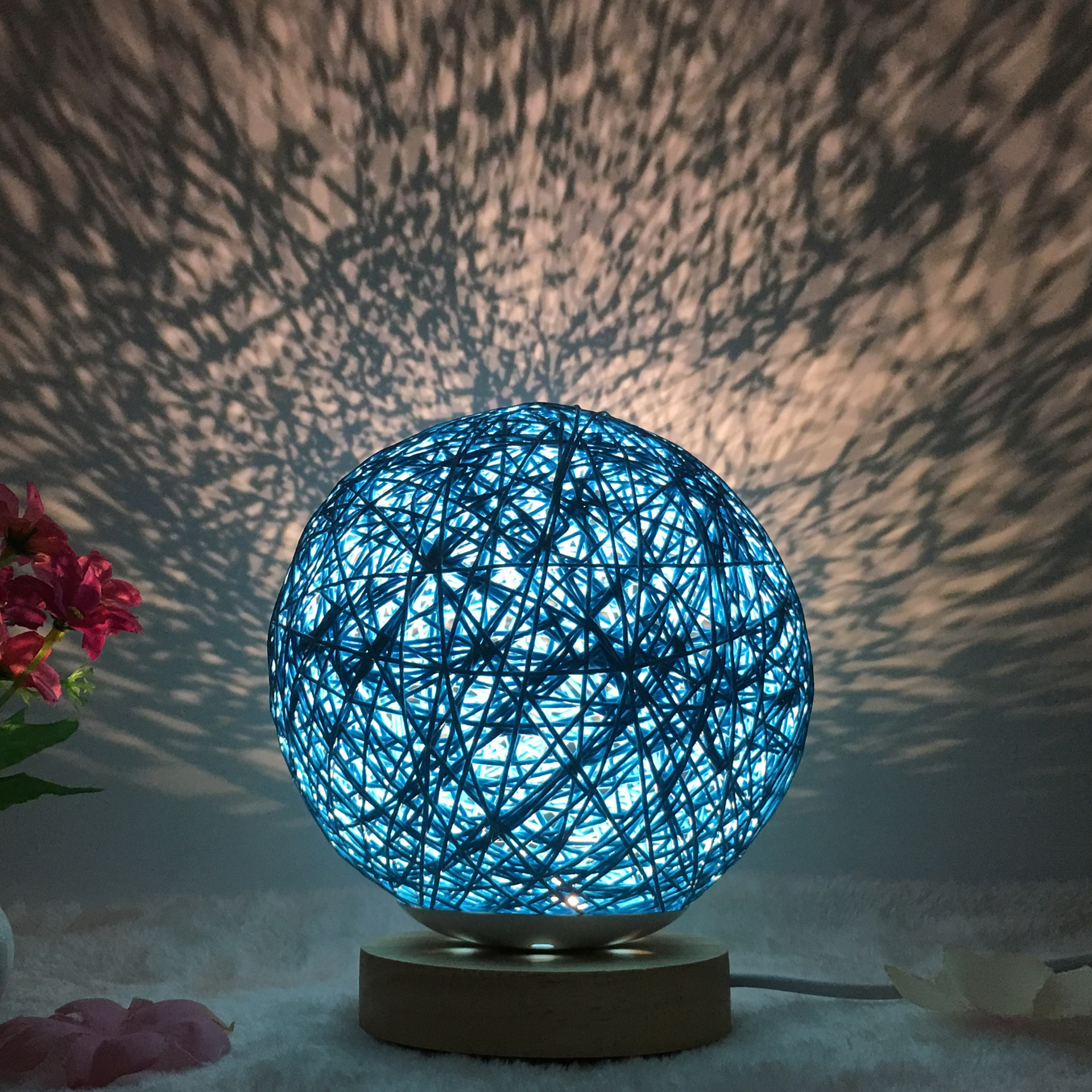 Blue Creative Rattan Ball Lamp with hand-knitted shade on wooden stand, casting artistic light patterns on the wall.