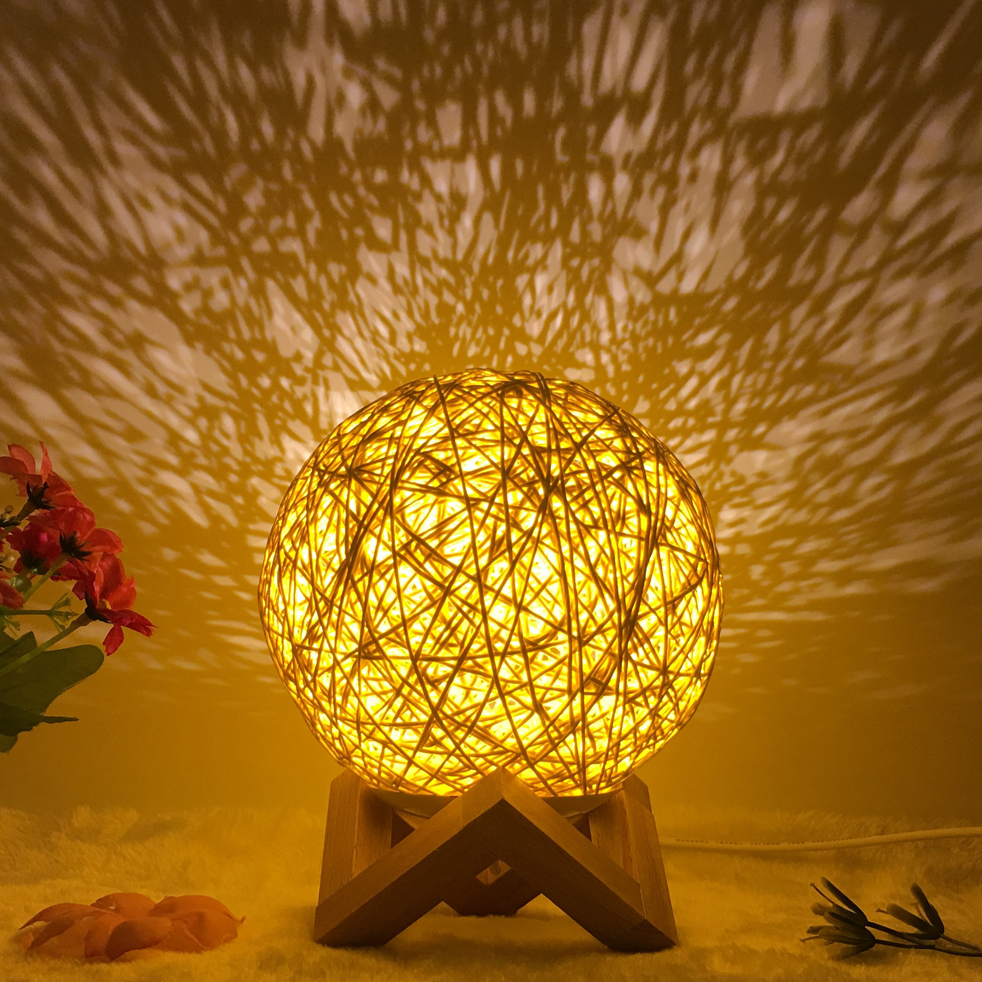 Warm glowing Creative Rattan Ball Lamp with hand-knitted shade on wooden stand, casting intricate shadows on the wall.