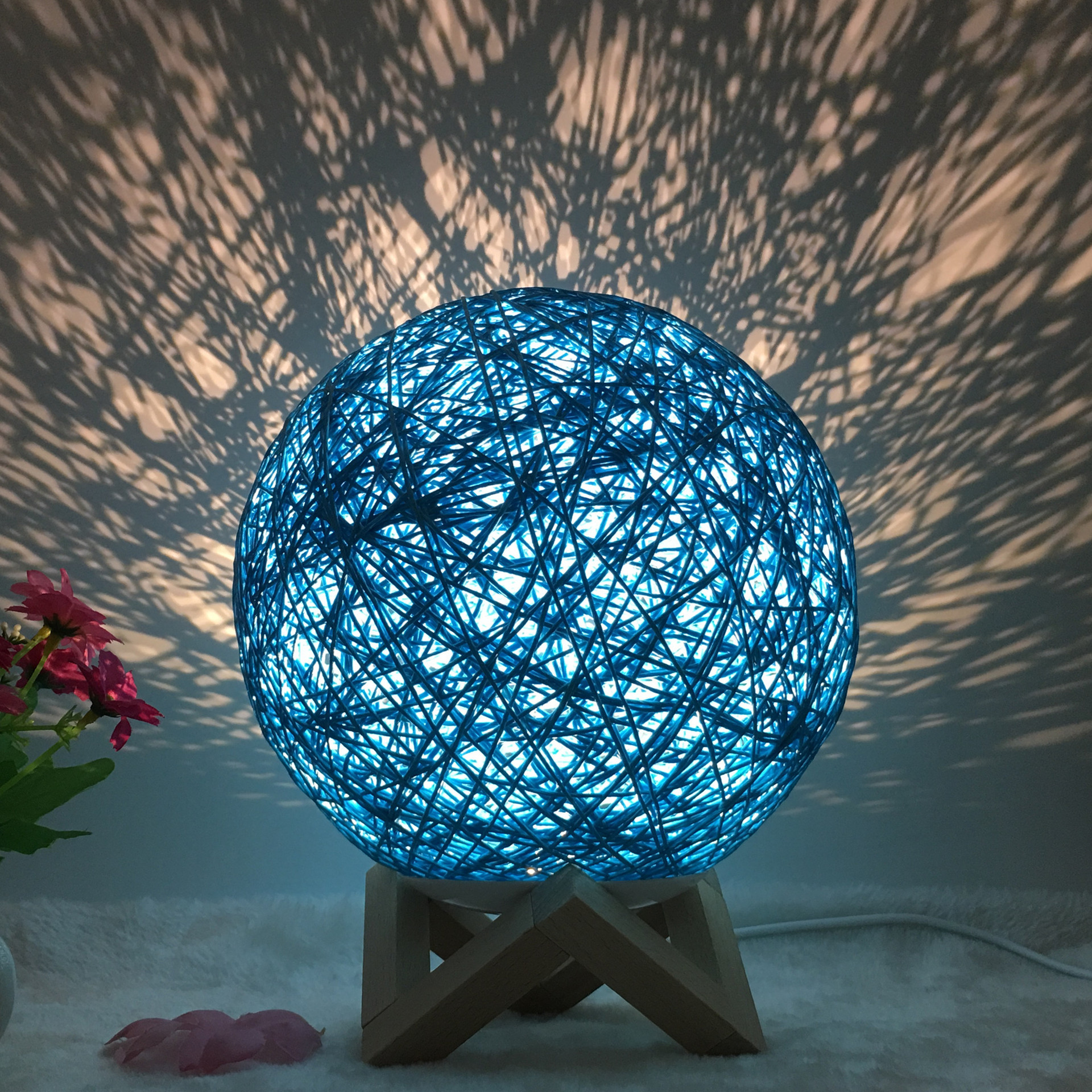Blue Creative Rattan Ball Lamp with hand-knitted shade on wooden stand, casting artistic light patterns on the wall.