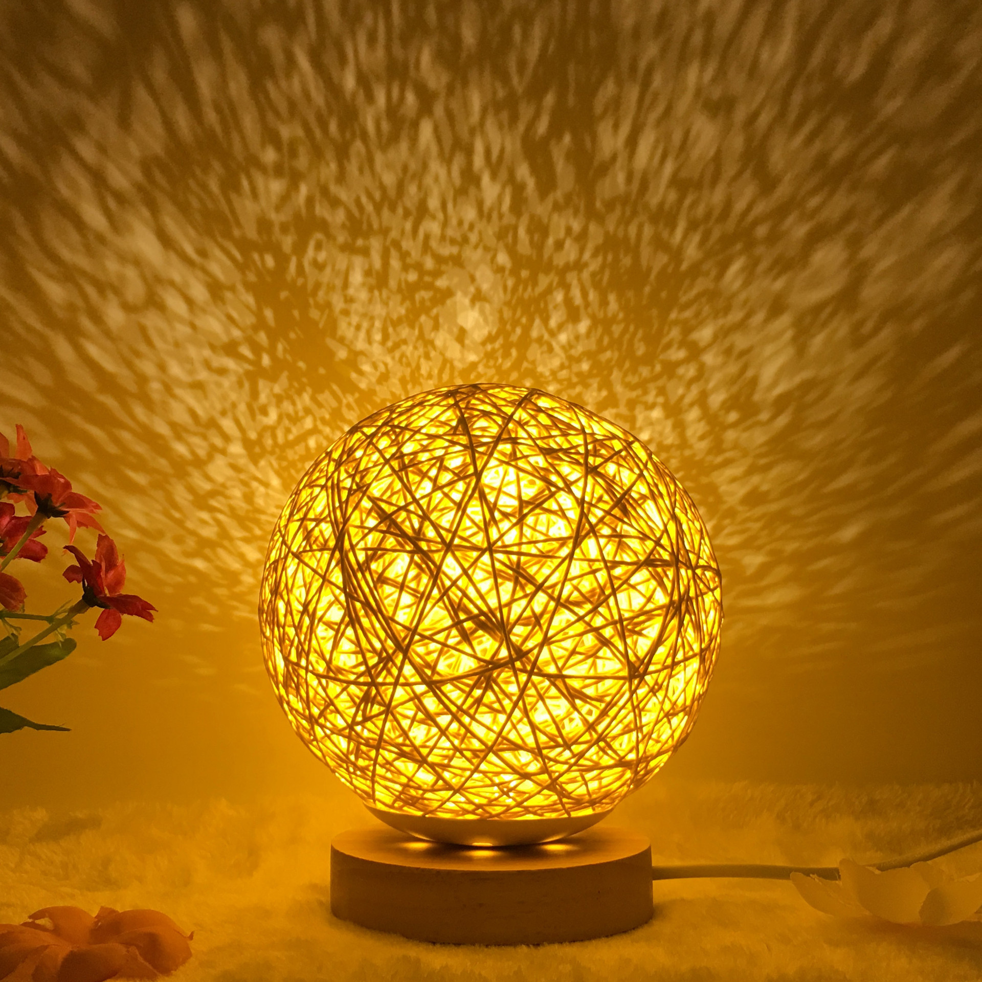 Warm glowing Creative Rattan Ball Lamp with hand-knitted shade on wooden stand, casting intricate shadows on the wall.