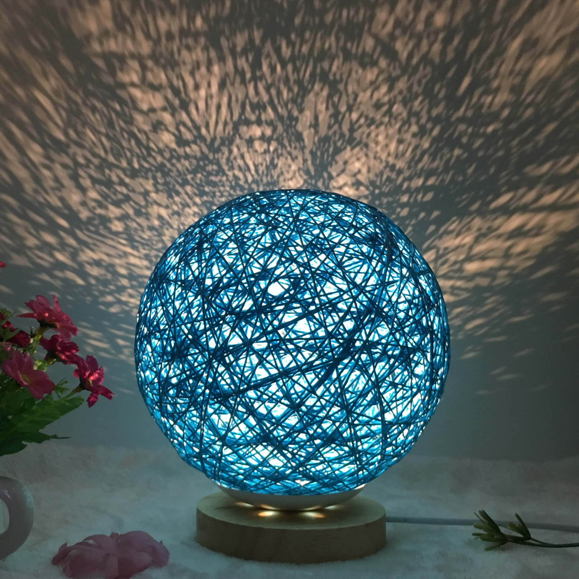 Blue Creative Rattan Ball Lamp with hand-knitted shade on wooden stand, casting artistic light patterns on the wall.