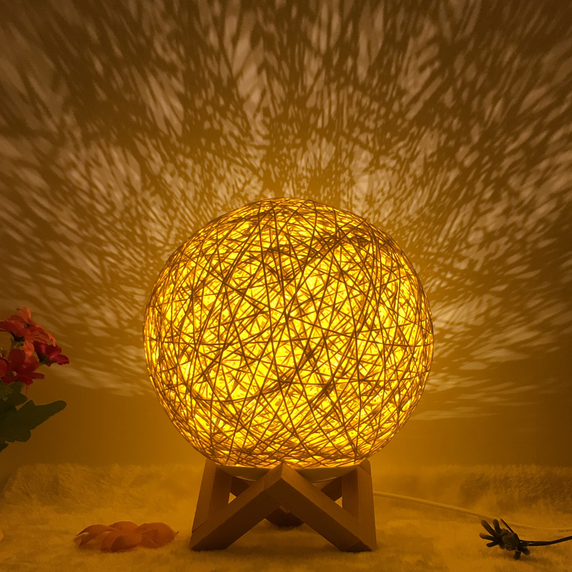 Warm glowing Creative Rattan Ball Lamp with hand-knitted shade on wooden stand, casting intricate shadows on the wall.
