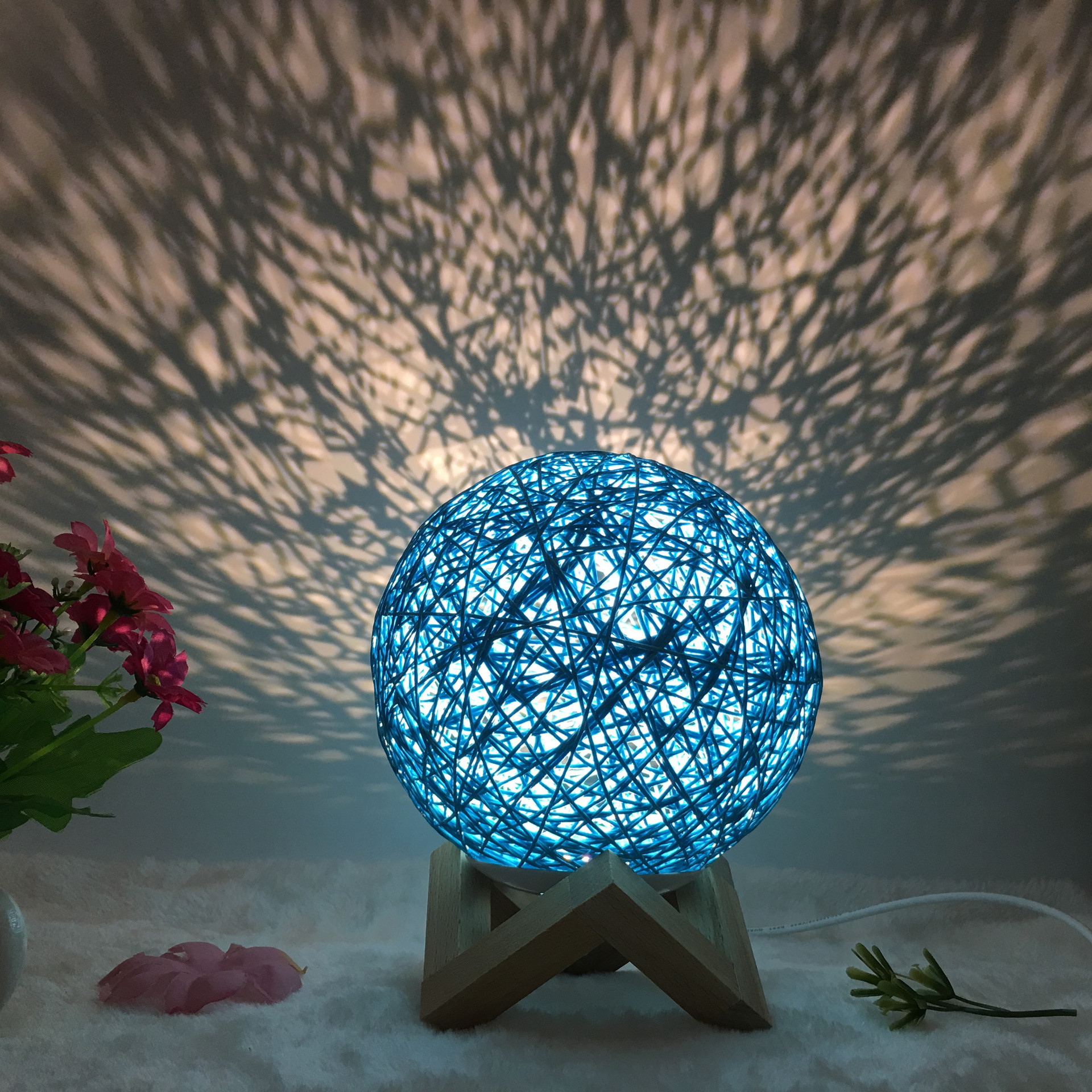Blue Creative Rattan Ball Lamp with hand-knitted shade on wooden stand, casting artistic light patterns on the wall.