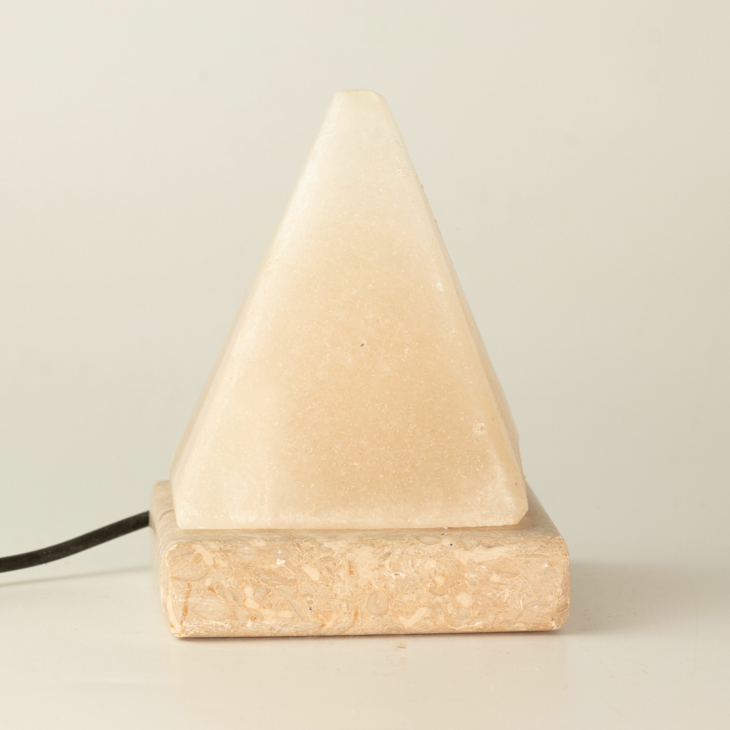White Himalayan salt crystal pyramid lamp on a salt base with a black cable